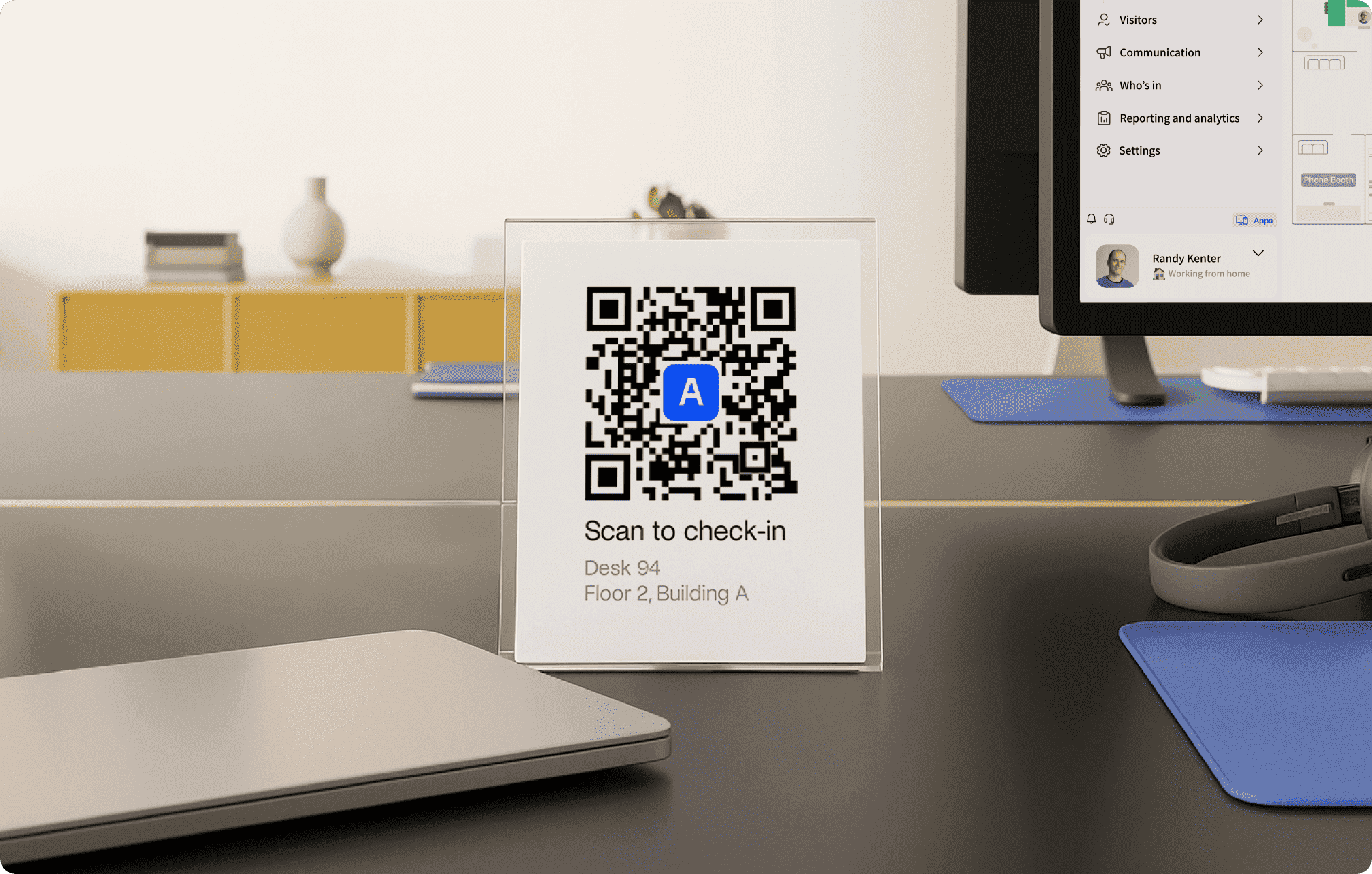 A desk setup with a QR code sign for check-in and a computer screen showing a workspace management application, Archie.