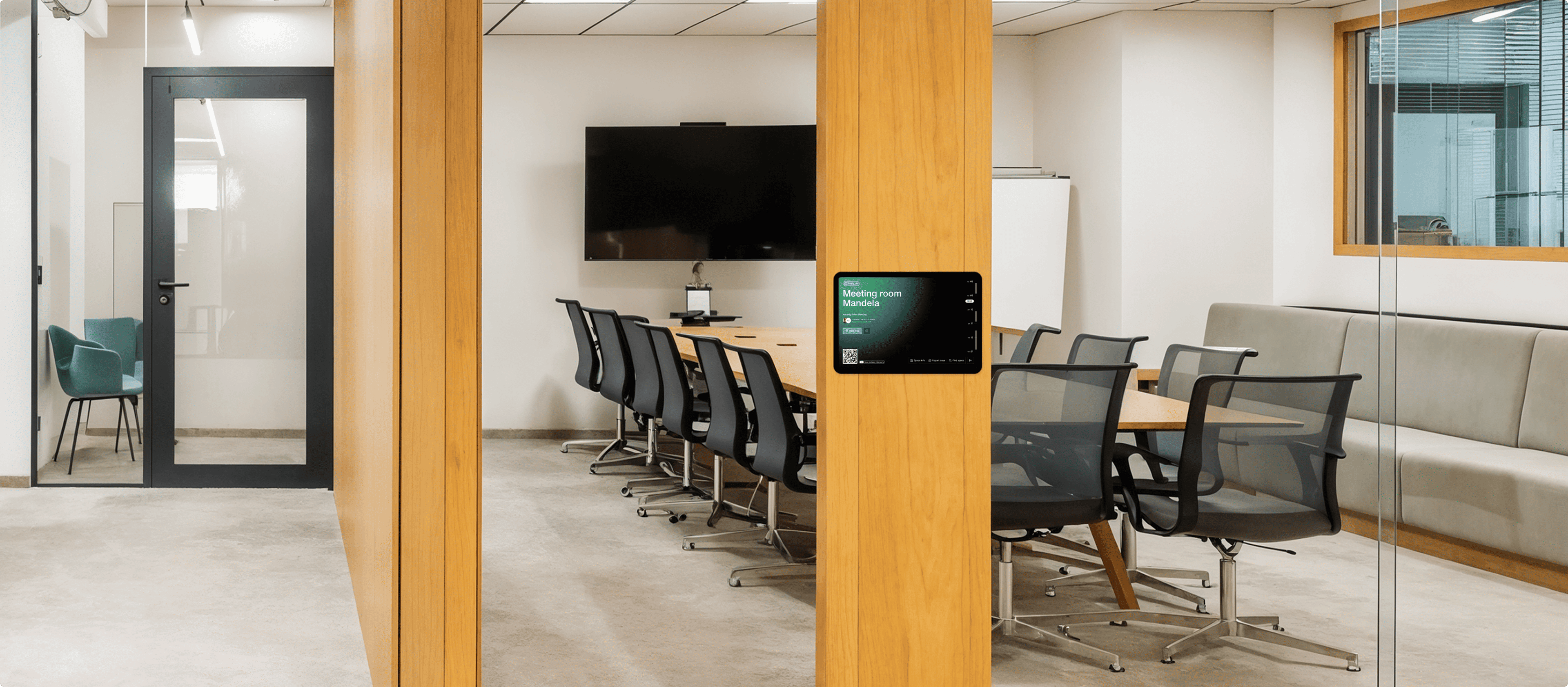 A tablet outside a spacious meeting room named "Mandela," showing the room's interior with a large table, chairs, a TV screen, and a whiteboard.