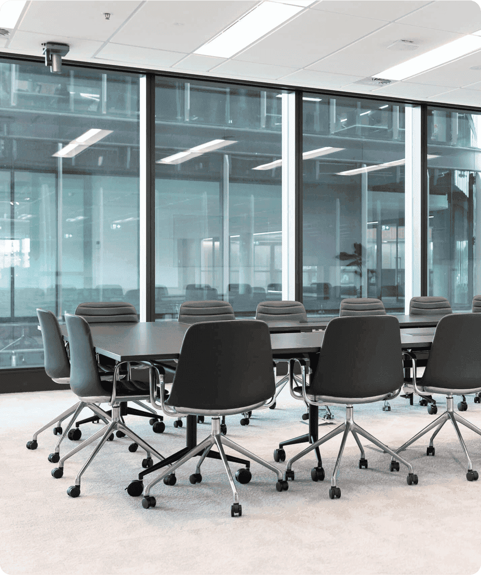 Conference room with a large table and multiple chairs, surrounded by glass walls.